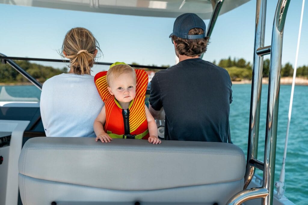 Young child in a life vest posing for a photo while parents pilot a Beneteau Flyer 9