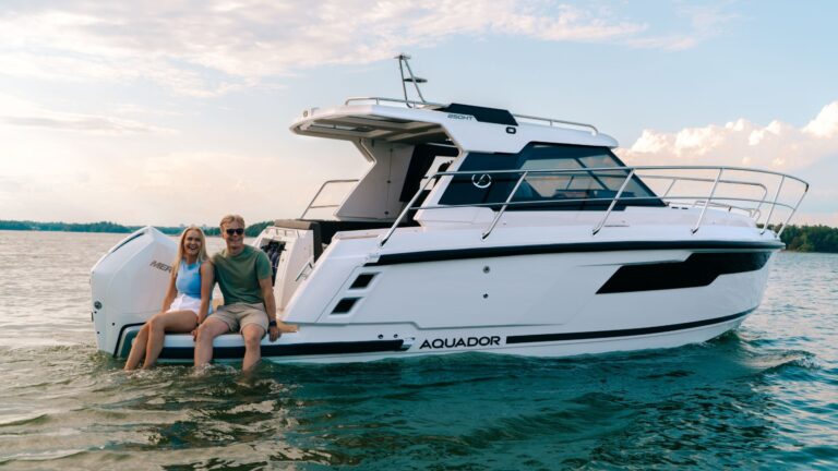 A man and a woman sitting on the back of an Aquador 250 HT with their legs in the water.